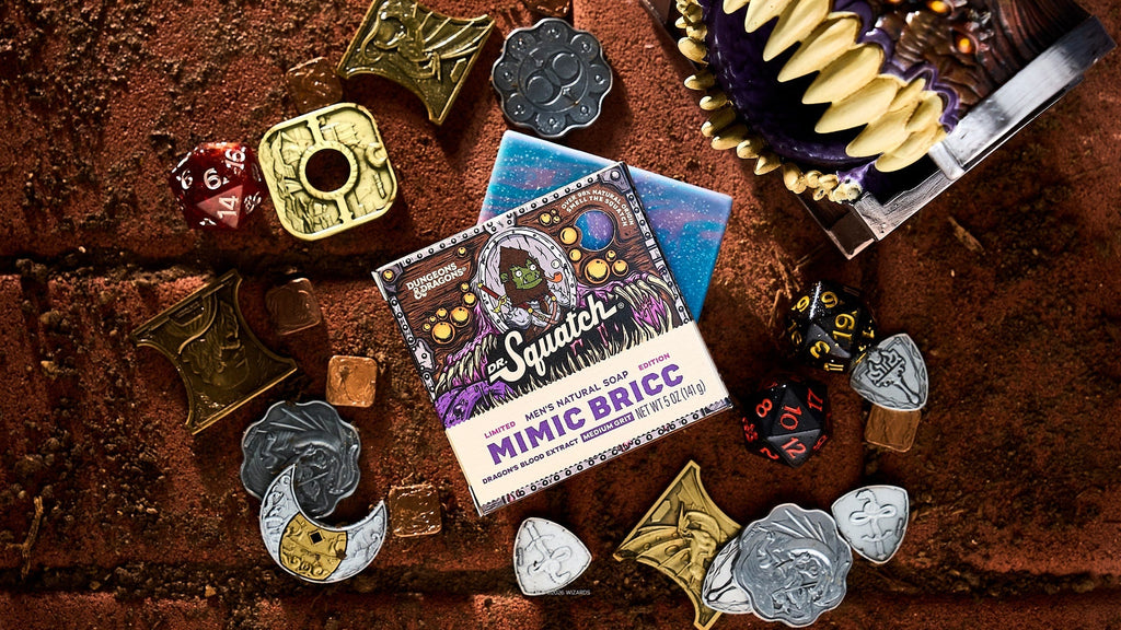 Mimic Bricc bar soap package surrounded by Dungeons & Dragons dice, metal miniature charms, and a starry blue pouch on brown textured surface.