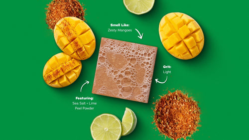 Mango exfoliating bar surrounded by fresh mangoes, lime slices, and cinnamon-chili powder on green background.